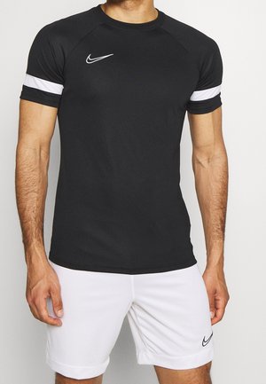 Mand iført sort sportsskjorte med korte ærmer med hvid stribe på ærmerne og hvide shorts med Nike-logoer på brystet og benet.