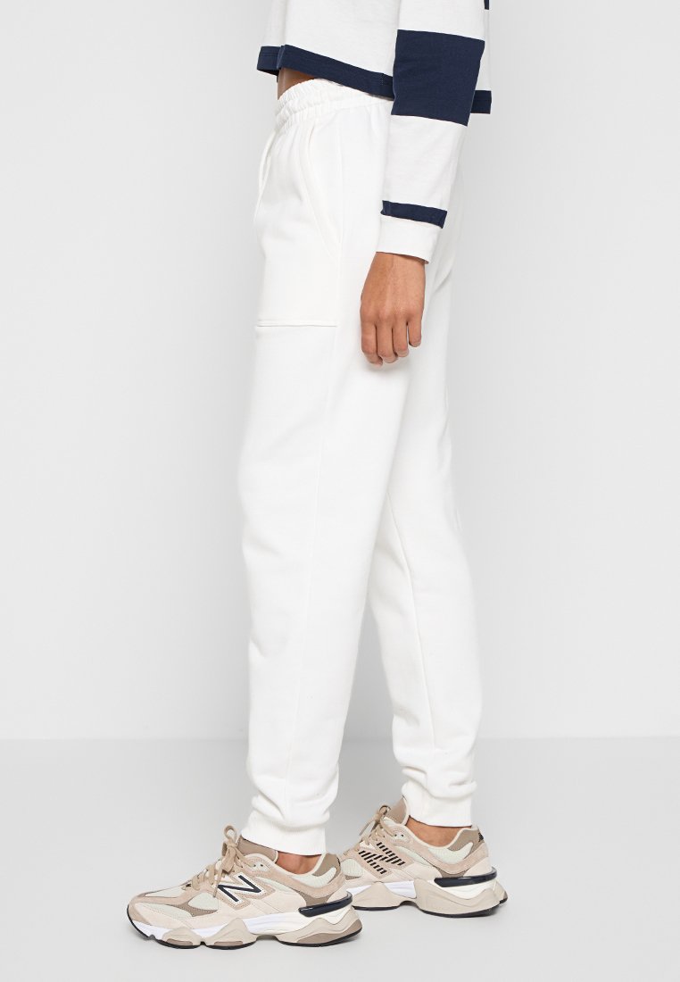 Weiße Sweatpants aus weichem Material mit einem elastischen Bund, ausgestattet mit Seitentaschen. Kombiniert mit beigen Sneakern mit dunklen Akzenten.