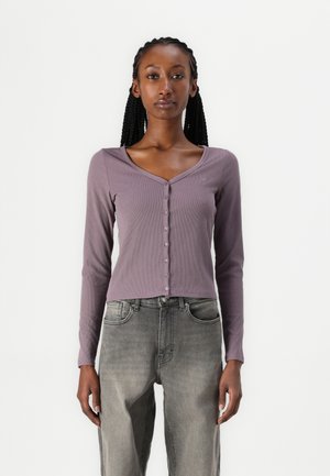 Langermet, knappet cardigan i ribbet lilla stoff, med V-hals og en tettsittende design, kombinert med falmede grå høyt midje jeans.