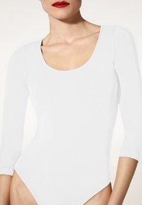 Weißes Langarm-Bodysuit mit einem runden Halsausschnitt. Hergestellt aus glattem, dehnbarem Stoff. Verfügt über hohe Beinausschnitte und eine enganliegende Silhouette.