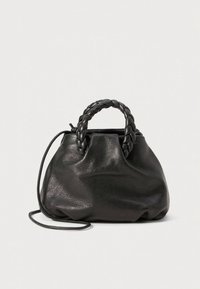 Černá kožená kabelka s pletenými rukojetmi a tenkým ramenním popruhem, ležící na světle šedém pozadí.