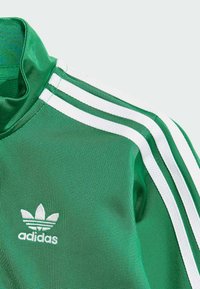 Zielona bluza sportowa adidas z białymi paskami, wysokim kołnierzem i wyszywanym logo. Faktura wydaje się gładka z delikatnym połyskiem.