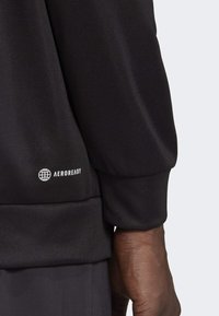 Svart sporttröja med elastiska muddar och Aeroready-logotyp. Slät, strukturerad tyg, något lös passform och synlig sömdetalj.