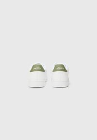 Bijele tenisice s glatkom teksturom, zelenim naglaskom na peti i jednostavnim dizajnom s "LACOSTE" logom na stražnjoj strani.