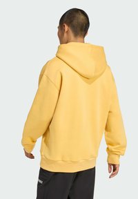 Gelber Hoodie mit großzügiger Kapuze, weicher Textur und gerippten Bündchen. Die Rückseite ist schlicht gestaltet, ohne Logos oder Muster.