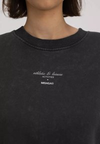 Zwarte sweatshirt met geribbelde ronde hals, met daarop witte tekst "athletic & leisure ACTIVITIES MISAGA®" aan de voorkant. Zachte textuur.