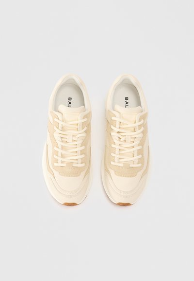 Cremfarbene und beiger Sneakers mit strukturiertem Design, ausgestattet mit Schnürsenkeln, einer gepolsterten Sohle und einem auffälligen Markenlogo auf der Innensohle.