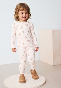 Ribikujulise tekstuuriga roosa lillemustriline pikkade varrukatega top ja retuuside komplekt, millele on lisatud pruunid libisevad kingad. Topil on lainelise servaga äärisdetailid.