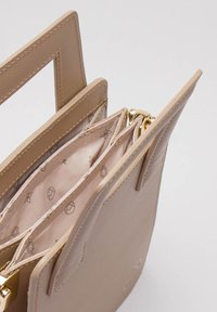 Beżowa skórzana torebka z złotymi akcentami, posiadająca wiele przegrod i wewnętrzną wzorzystą podszewkę. Strukturalny design z kanciastymi uchwytami.