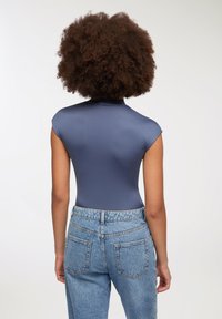 Granatowy, dopasowany body z wysokim kołnierzem i rękawami typu cap, połączony z jasnoniebieskimi spodniami z wysokim stanem, posiadającymi tylne kieszenie.