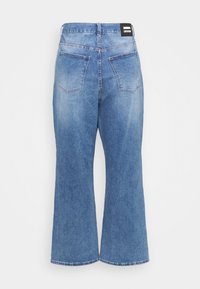 Jean large en denim bleu vu de dos avec deux poches et un patch de marque noir sur la ceinture.