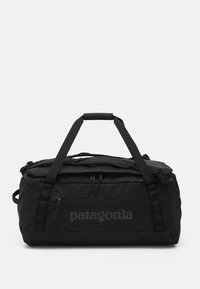 Black duffel bag with a textured exterior, dual top handles, zipper closure, and subtle Patagonia logo on the side. Compact and durable design.