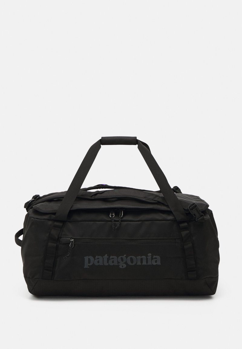 Black duffel bag with a textured exterior, dual top handles, zipper closure, and subtle Patagonia logo on the side. Compact and durable design.