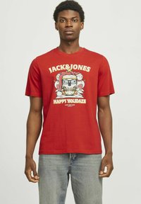 Camiseta de algodón roja con un estampado gráfico de una calavera usando gafas, rodeada de pájaros y el texto "JACK&JONES HAPPY HOLODaze." Mangas cortas.