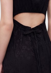 Gros plan du dos d'une personne portant une robe noire avec une découpe et un nœud noué à la taille avec des motifs floraux subtils.