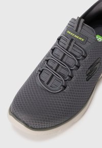Sivé tenisky Skechers s priehľadnou vrchnou časťou, čiernymi elastickými šnúrkami, označeným pútkom a bielou podrážkou, viditeľné na bielom pozadí.