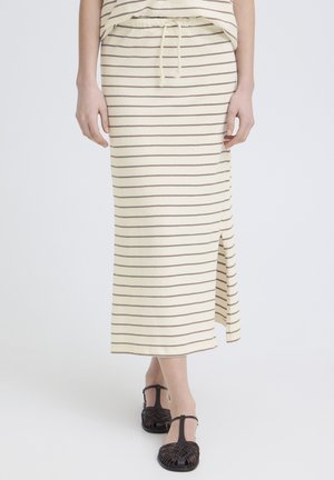 Person wearing a cream midi skirt with thin horizontal brown stripes and a side slit, paired with black woven T-strap sandals.