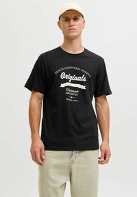 Czarny bawełniany t-shirt z białym nadrukiem; krótki rękaw, okrągły dekolt, luźny krój. Nosi się z jasnoniebieskimi dżinsami.