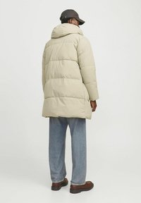 Beige pufferjakke med hætte, quiltet design og høj krave. Sammen med lyseblå jeans og brune sko. Enkel, funktionel stil.