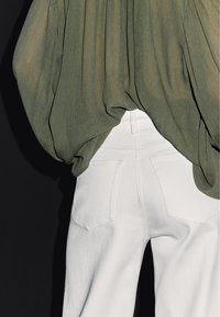 Blusa trasparente color verde oliva con maniche voluminose, abbinata a jeans di denim bianchi a vita alta con tasche posteriori e vestibilità aderente.