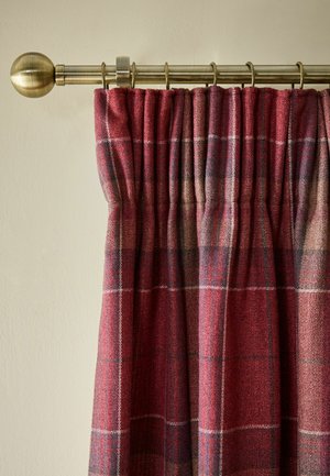 Rot- und violett karierter Vorhang, der an einer goldfarbenen Metallgardinenstange mit rundem Abschluss vor einer beigen Wand hängt.