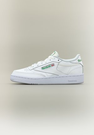 Zapatilla baja blanca de Reebok con logo verde y bandera del Reino Unido en el lateral, suela blanca y cordones, mostrada desde el lado exterior sobre un fondo neutro.