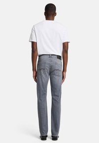 Jeans grigi con taglio dritto, con tasche posteriori e dettagli di cucitura. Abbinati a una t-shirt bianca semplice. Accentato da una cintura nera.