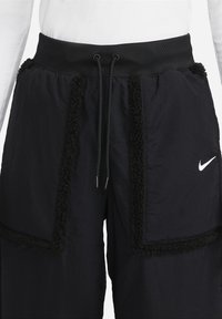 Czarne spodnie sportowe z teksturowanym, puszystym wykończeniem przy kieszeniach i bokach, z elastycznym pasem z regulowanym sznurkiem oraz logo Nike.