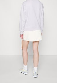 Sweatshirt violet clair avec un ourlet et des poignets côtelés, associé à une jupe évasée blanche. Baskets beiges et pastel avec des chaussettes blanches.