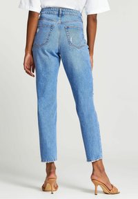 Jasnoniebieskie spodnie o wysokim stanie z prostymi nogawkami, z tylnymi kieszeniami i postrzępionymi nogawkami, w połączeniu z beżowymi sandałami na wysokim obcasie.