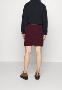 Černá mikina s volánovým límcem spárovaná s vínovou pletenou sukní. Hnědé šněrovací boty s robustními černými podrážkami.