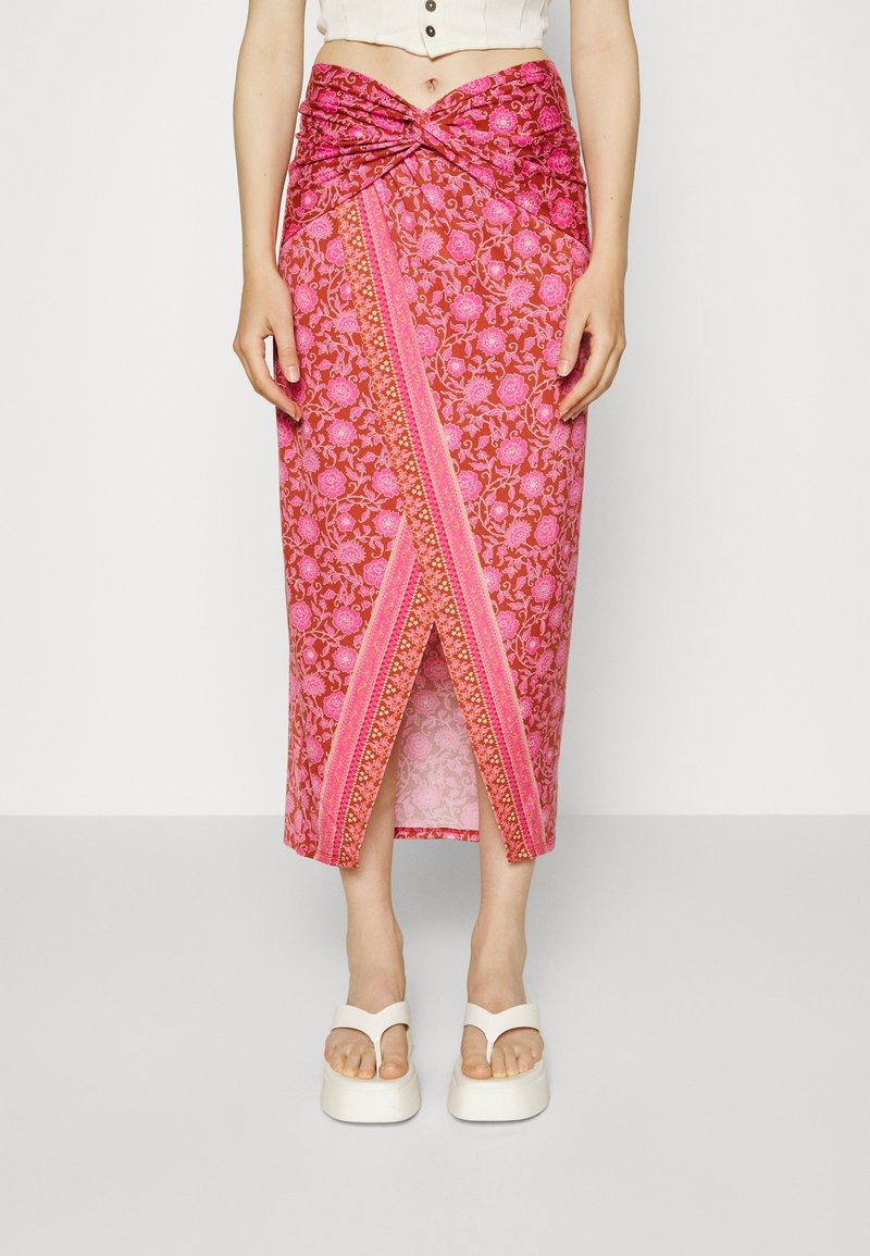 Lång rosa kjol med blommönster, en twist-framdesign, hög slits på sidan och kontrasterande kanter. Bärs med vita platåsandaler.