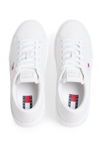 Λευκά αθλητικά παπούτσια από λείο συνθετικό υλικό, με στρογγυλή μύτη, κορδόνια στο μπροστινό μέρος και ετικέτα με κόκκινες, λευκές και μπλε λεπτομέρειες.