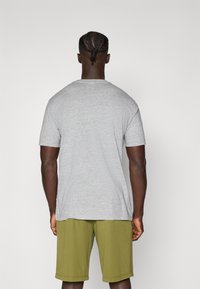 Grå kortærmet t-shirt med rund hals, præsenteret med grønne atletiske shorts. Stoffet ser blødt ud med en glat tekstur.
