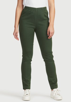 Grüne, schmal geschnittene Hose aus Baumwollmischgewebe mit elastischem Bund. Verfügt über frontale Taschen und eine glatte Textur. Kombiniert mit weißen Sneakers.