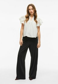 Blusa bianca a maniche corte con maniche arricciate e scollo a V, abbinata a pantaloni neri a gamba larga in un tessuto liscio.