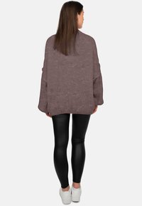 Pull tricoté surdimensionné mauve avec manches longues, ourlet côtelé et fini texturé, associé à des leggings noirs et des baskets blanches.