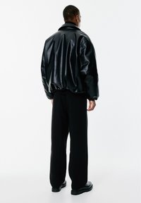 Veste bomber noire, brillante, avec un ourlet et un col côtelés, associée à un pantalon noir ample et des bottes noires robustes.