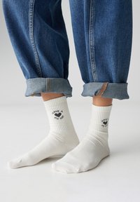 Calzini bianchi a costine di lunghezza media, con testo nero e grafica a forma di cuore con la scritta "Have a Nice Day". Indossati con jeans di denim risvoltati.