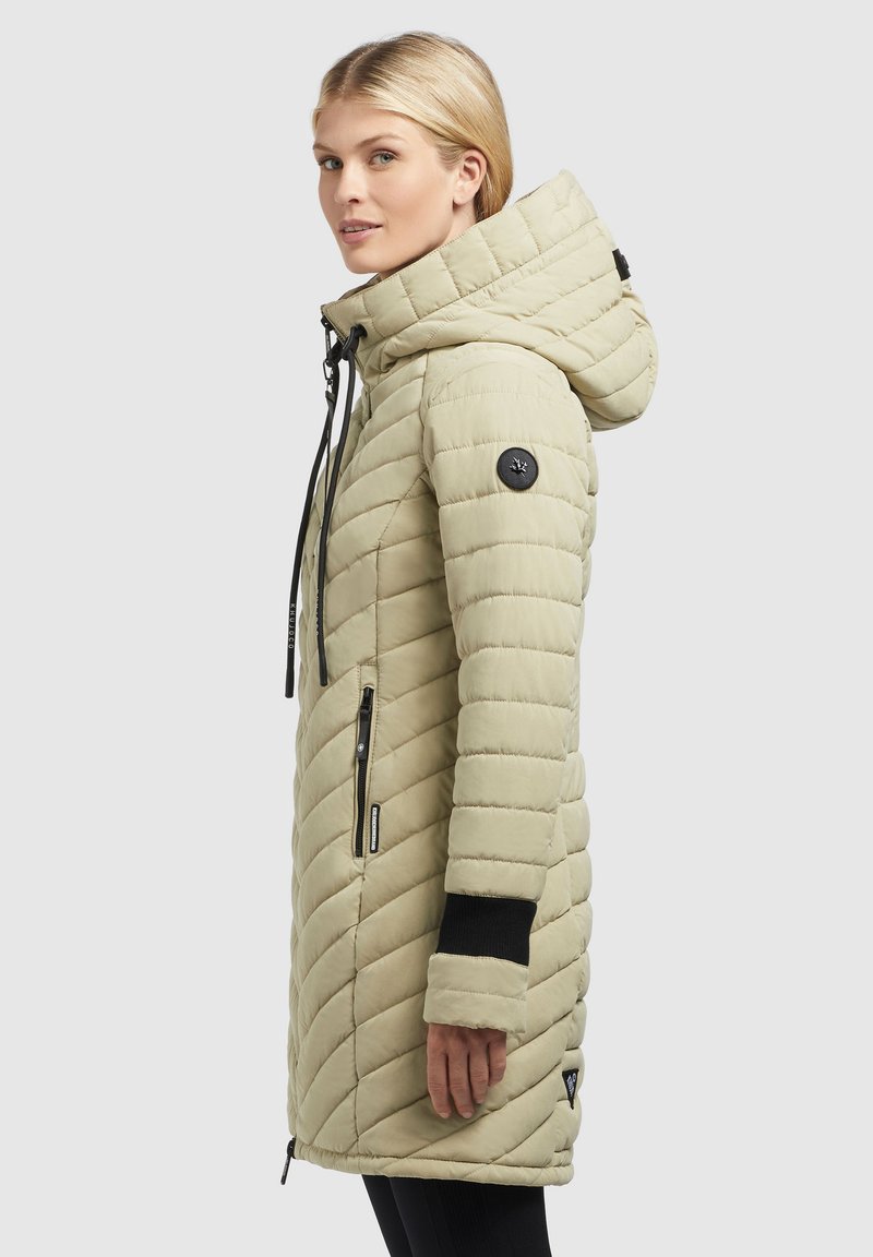 Hellbeige gesteppter langer Mantel mit Reißverschluss vorne, verstellbarem Kapuzenrand, schwarzen Akzenten und seitlichen Taschen mit geschwungenen Nähten und strukturiertem Stoff.