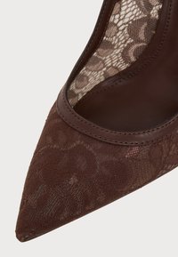 Chaussure marron à lacets avec bout pointu, garniture en cuir et doublure en tissu à motifs à l'intérieur.
