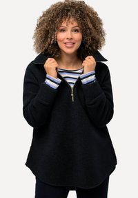 Pullover in pile nero con mezza zip, colletto alto e spalle scese. Presenta uno strato interno a righe visibile all'escursione del collo. Texture morbida.