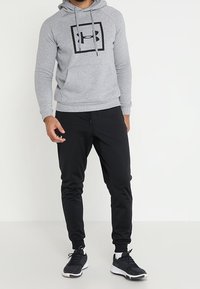 Sudadera con capucha gris y logo negro en un cuadrado, combinada con joggers ajustados negros y zapatillas deportivas negras. Ropa deportiva casual.