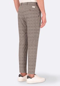 Pantaloni a quadri marroni con vestibilità sartoriale, dotati di tasche laterali, una tasca posteriore singola e un piccolo etichetta sulla vita. Abbinati a sneakers bianche.