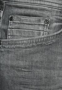 Šedé denimové džíny se zadní kapsou s viditelným švem a detaily z černého kovového knoflíku. Textura vypadá jako tkaná a je mírně opotřebovaná.