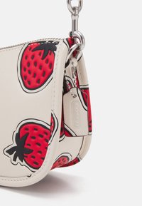 Crèmekleurige leren tas met rood aardbeienpatroon, zilverkleurige hardware en ketting, voorzien van een ritssluiting en een getextureerde, afgeronde vorm.