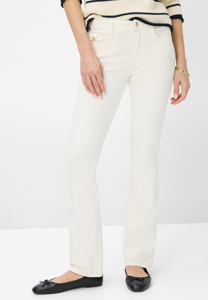 Roomkleurige rechte jeans van zachte stof, met een achterzak en gouden hardware. Draagt met zwarte ballerina's.
