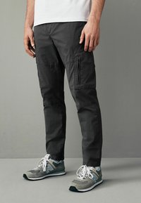 Pantaloni cargo de culoare gri închis, cu un buzunar cu fermoar, talie elastică și un design cu tăietură dreaptă. Așortați cu adidași gri cu accente albe.