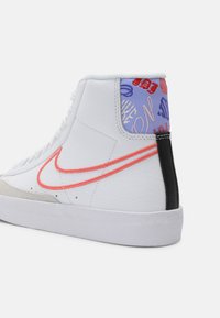 Zapatilla alta en cuero blanco con detalles en rosa y rojo, puntera de ante gris, y tela estampada azul en la parte trasera. Suela de goma.