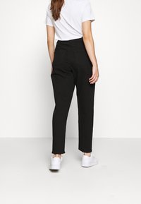 Pantalones negros de talle alto con pierna recta, dos bolsillos traseros y una textura suave, combinados con zapatillas deportivas blancas y una camiseta blanca.